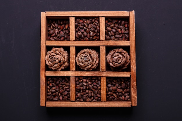 Pine nuts and cones in a wooden box on a black slate. Top view.
