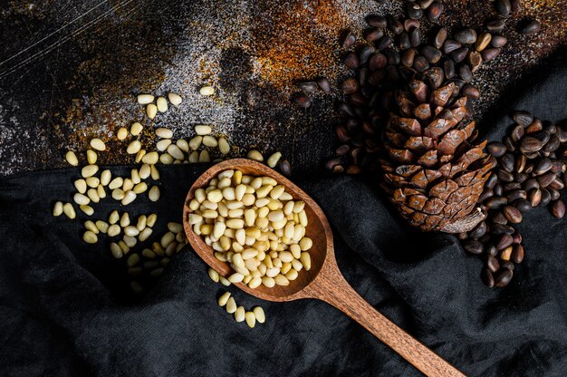 Pine nuts in the spoon and pine nut cone. Organic food. Black background. Top view