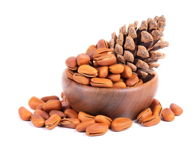 Pine nuts in wooden bowl isolated on white background pine cones and heap of roasted pine nuts in