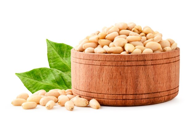 Pine nuts in a wooden plate with green leaves close-up on a white background. Isolated