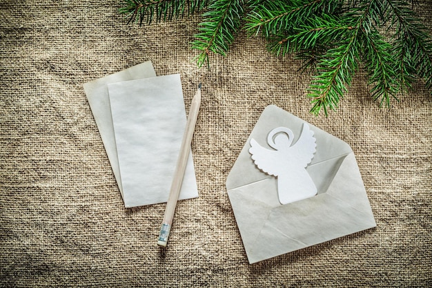 Pine tree branch envelope letter pencil angel on sacking background.