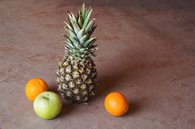 Pineapple, apple and oranges on wooden background.