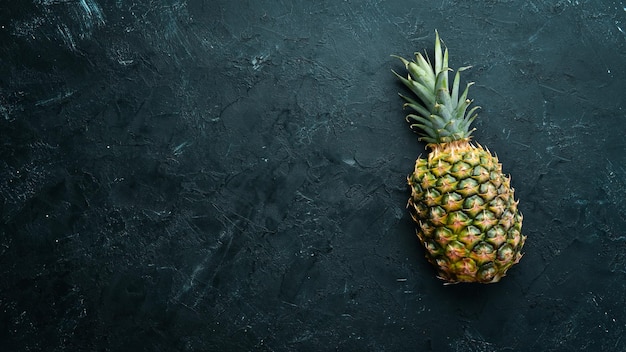 Photo pineapple on a black stone table tropical fruits top view free space for your text