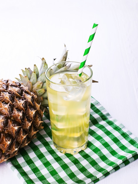 Photo pineapple cocktail with ice and green straw, on a white table. summer fruit mood.