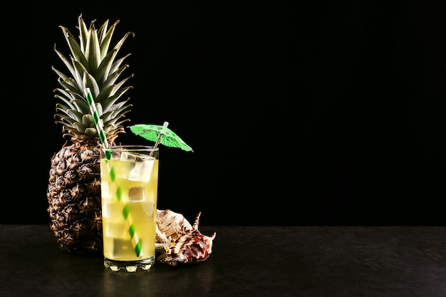 Pineapple cocktail with ice tube and umbrella on a black Tropical fruit and shells, summer mood in a dark style.