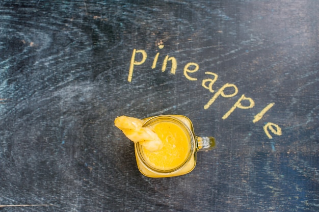 Pineapple cocktail with a slice of on wooden background and inscription in chalk . Tropical concept