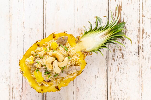 Photo pineapple fried rice with pork egg garlic onion spring onion pepper and curry powder cashew nut on top on old white wood background top view khao pad sapparod thai food
