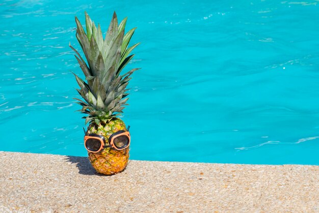 Pineapple fruit with rubber goggles for swimming in the water stands on rubber slippers on the backg