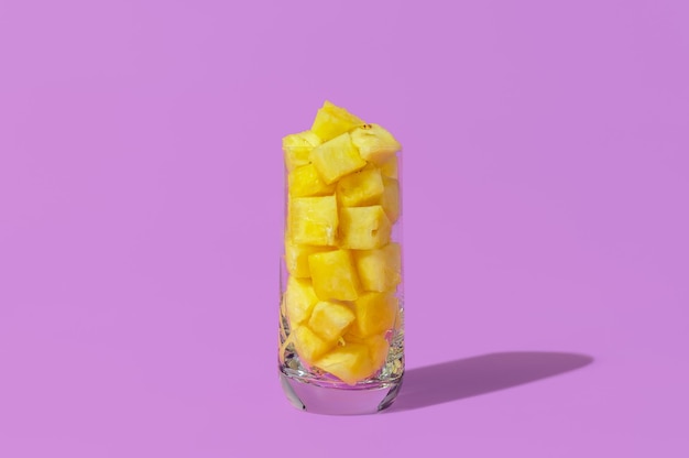 Pineapple juice concept Glass with pineapple cubes isolated on a purple background