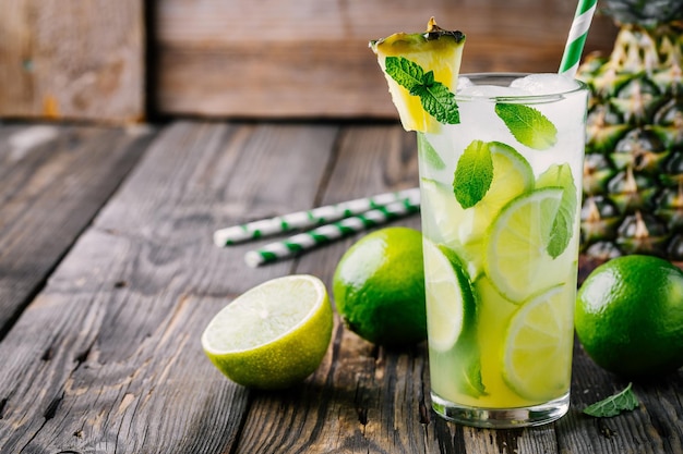 Pineapple Mojito cocktail with lime slices and mint in glass on wooden background