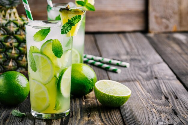 Sangria mojito all'ananas con fette di lime e menta in vetro su fondo di legno