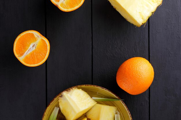 Pineapple pieces and orange halves on black wooden boards Pineapple fruit and oranges on dark background