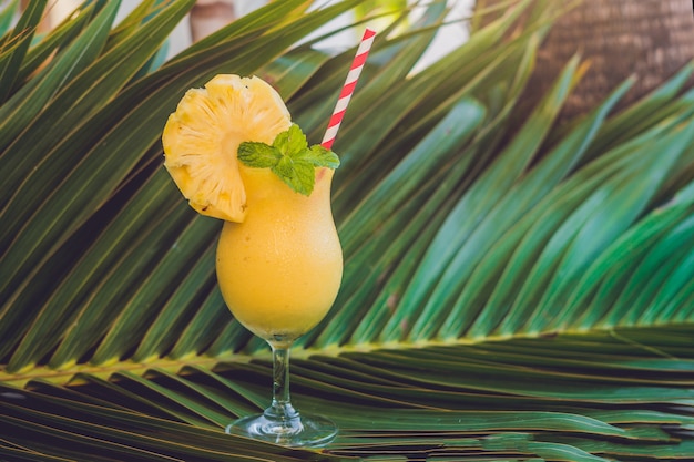 Pineapple and pineapple smoothies against the surface of a branch of a palm tree