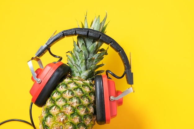 Pineapple in red retro headphones on yellow background