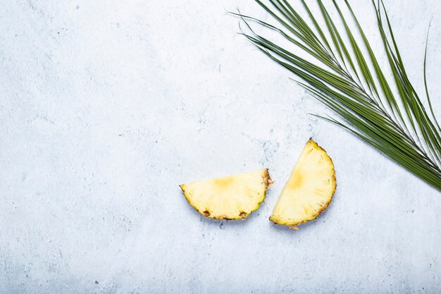 Pineapple slices and palm leaf on a concrete surface. Top view, flat lay.