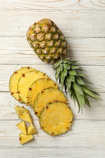 Ananas e fette su fondo di legno bianco