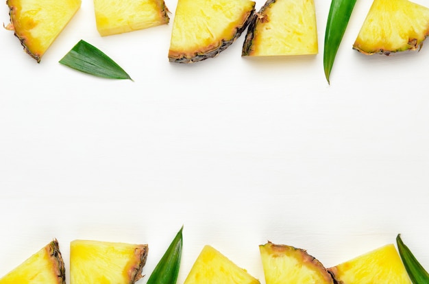 Pineapple slices with green leaves of pineapple on a white wooden background frame.