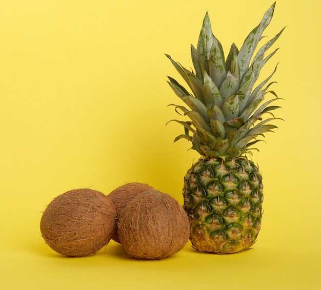 Pineapple and whole brown coconuts on a yellow background, healthy fruits