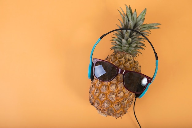 Photo pineapple with sunglasses and headphone on orange background. fruit summer concept.