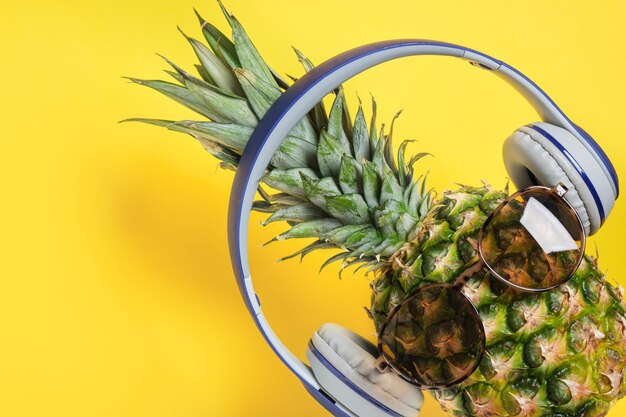 Pineapple with sunglasses and headphones on yellow background