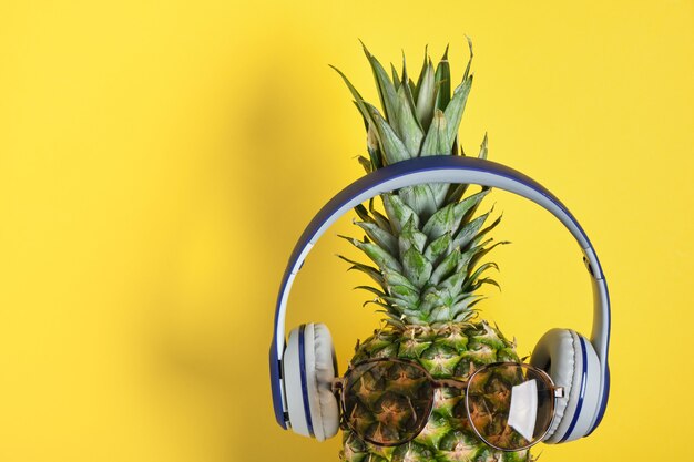 Pineapple with sunglasses and headphones on yellow background