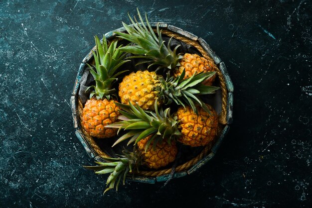 Pineapples in a wooden box. Ripe baby pineapple. Tropical fruits. Top view. Free space for text.