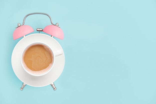 Pink alarm clock and coffee cup on blue copyspace. Breakfast time concept. Minimal style