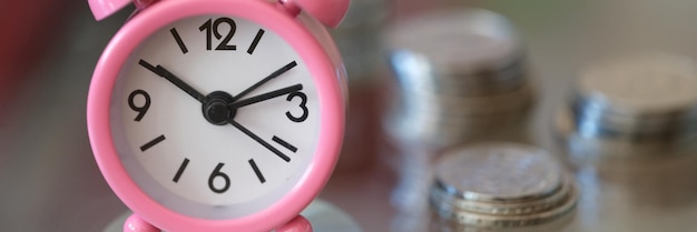 Photo pink alarm clock compass and stacks of coins closeup