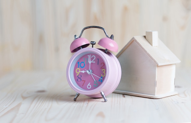 Pink alarm clock and a house place on the wooden table 