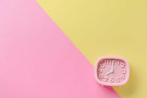 Pink alarm clock lying on yellow surface background. Top view.