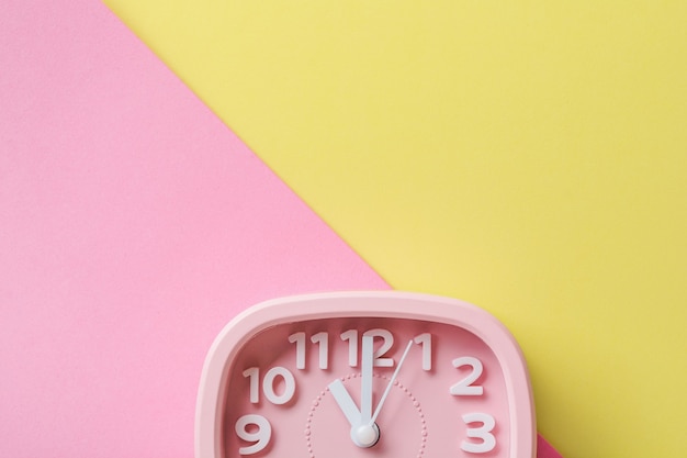 Pink alarm clock lying on yellow surface background. Top view.