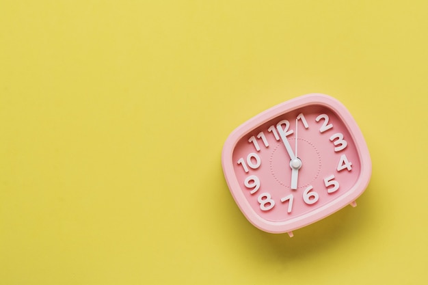 Pink alarm clock lying on yellow surface background. Top view.