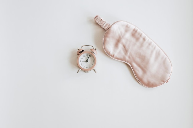 Pink alarm clock and a sleep mask on a white background