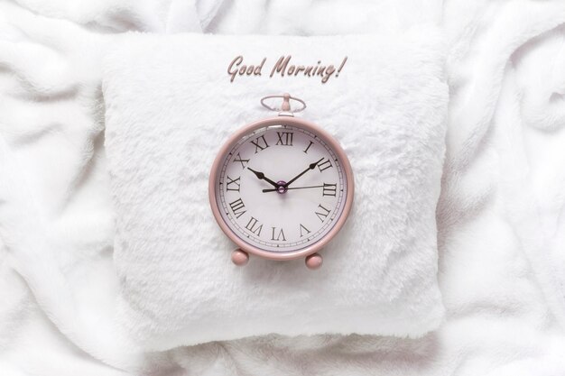 Pink alarm clock on a white pillow on a white blanket.