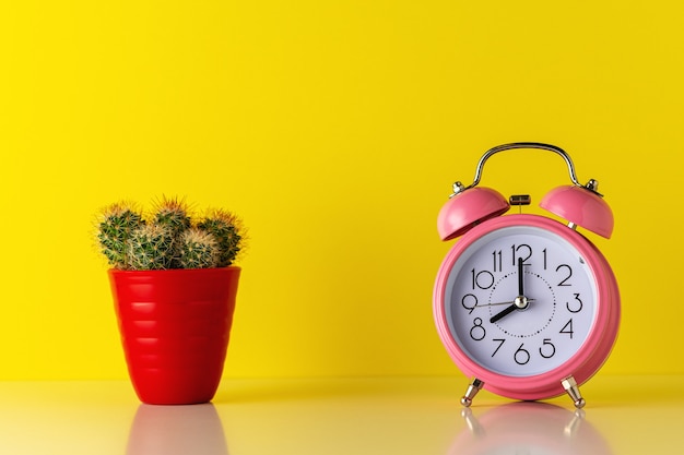 Pink alarm clock with cactus in pot on wooden desk