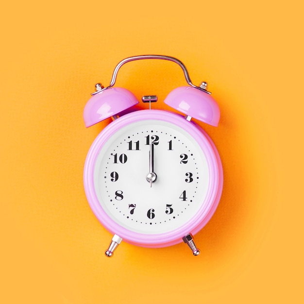 Pink alarm clock on yellow background.