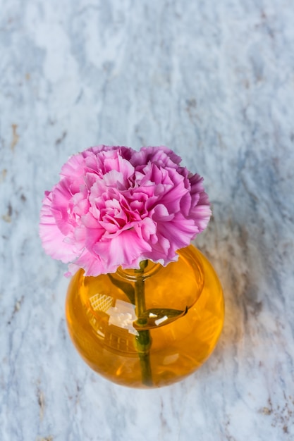 Pink artificial flower in brown round bottle on marble floor.