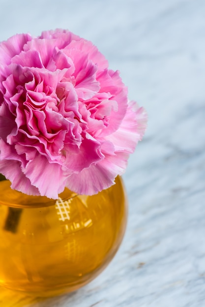 Pink artificial flower in brown round bottle on marble floor.