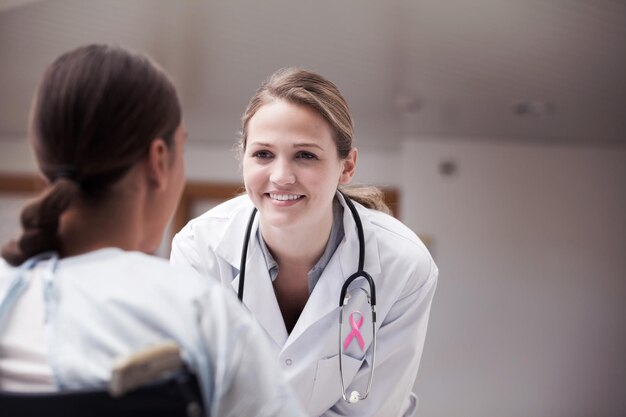 Pink awareness ribbon against smiling doctor looking at a patient on a wheelchair