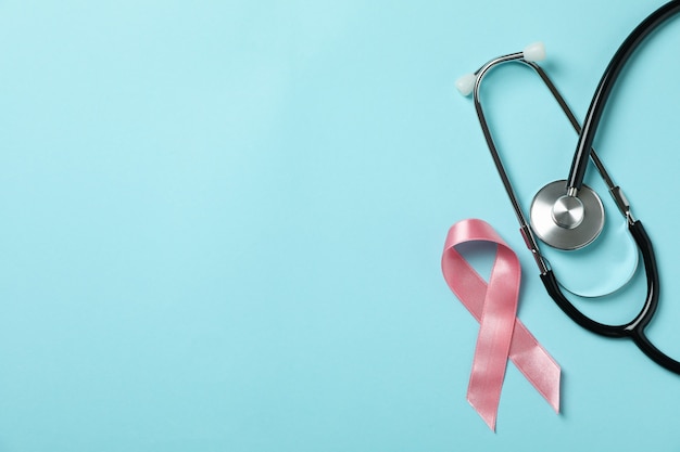 Pink awareness ribbon and stethoscope on blue background