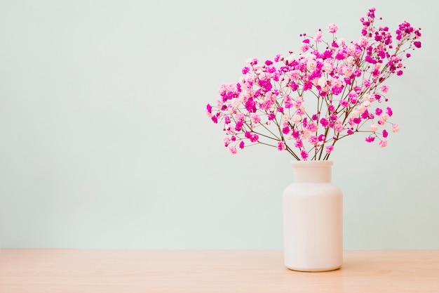 写真 色のある背景の木製の机の上に白い瓶のピンクのbaby's-breathの花
