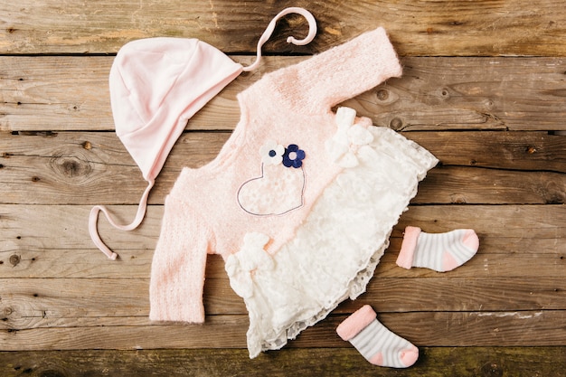 Photo pink baby's dress with headwear and pair of socks on wooden table