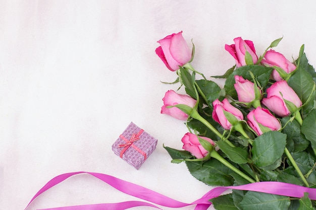 Su uno sfondo rosa un mazzo di rose rosa, una scatola con un regalo e un nastro rosa