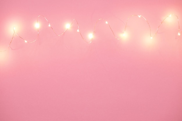 Pink background with Christmas lights and copying space. Christmas garland. New Year.