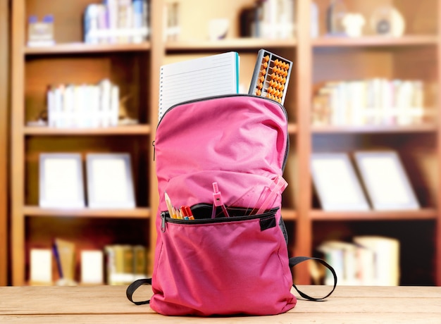 Pink backpack with book and different stationery on the wooden table