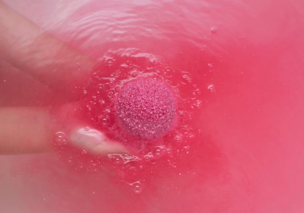 Pink bath bomb in her hands, foaming in the water, close-up. A place to copy.