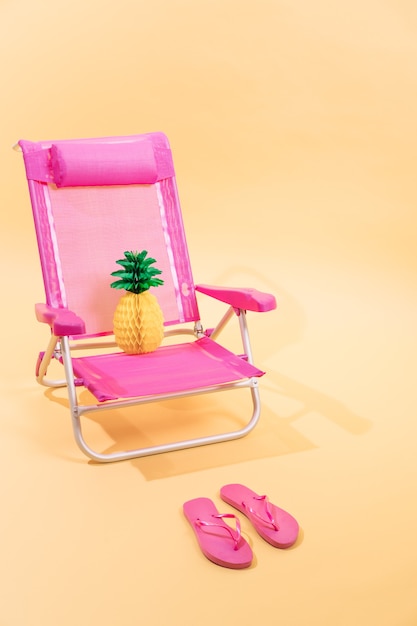 Pink beach chair with a paper pineapple on top of it and pink flip flops