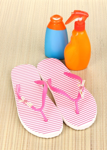 Pink beach slippers and sunscreen on mat