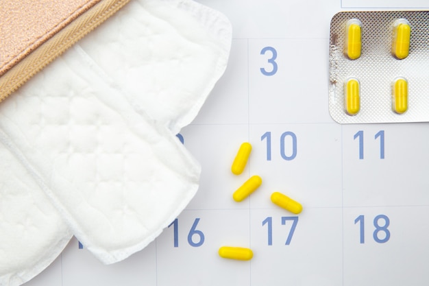 毎日綿の生理用ナプキンとホルモン避妊薬をカレンダーに載せたピンクの美容師。