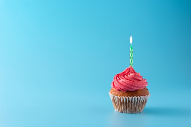 Pink birthday cupcake with green candle on blue background